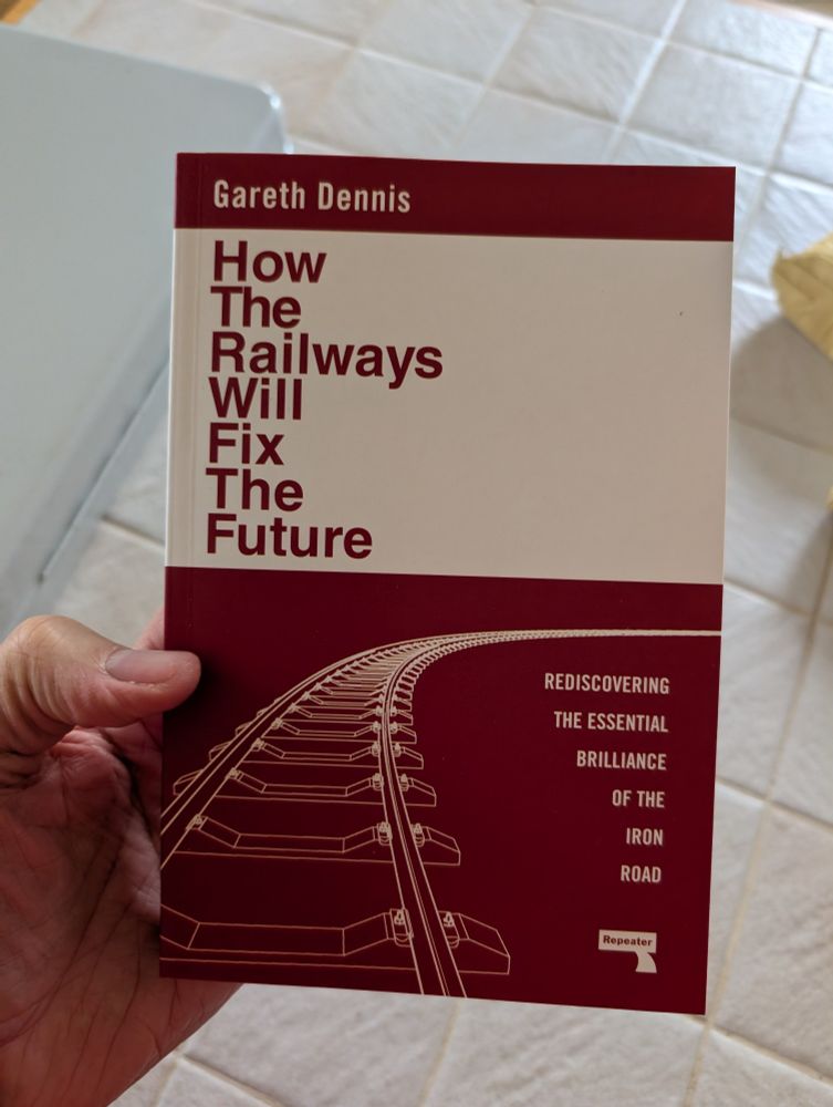 A hand holds up a paperback copy of Gareth Dennis's book How The Railways Will Fix The Future.