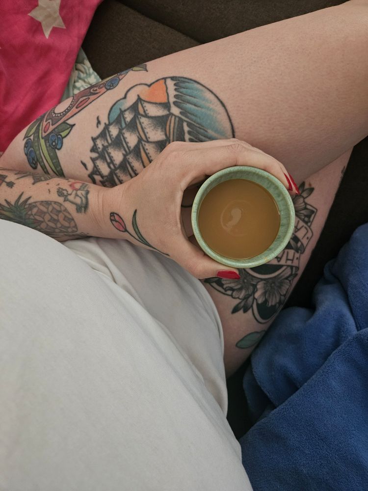 Kaffee im Schoß einer Frau. Man sieht bunte Tätowierungen.
