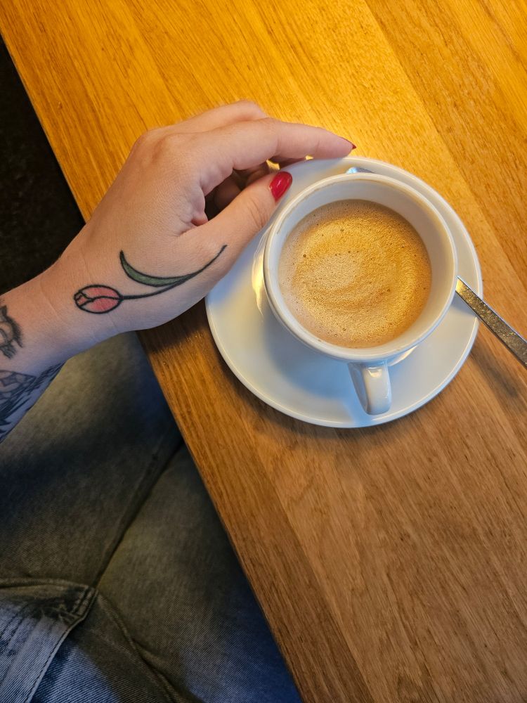 Hafercappucino in einer weißen Tasse, festgehalten von einer Frauenhand.