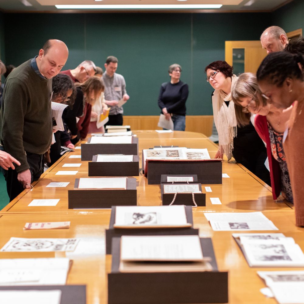 People standing around a long table, looking down at a variety of books and papers laid out.