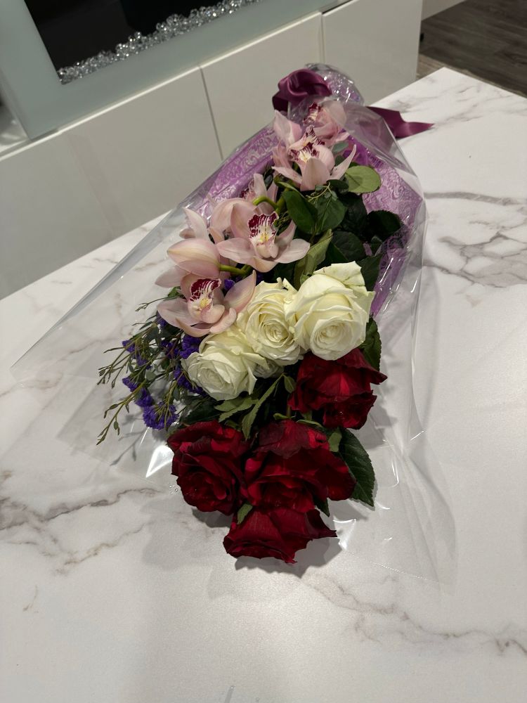 Boquet of flowers- red roses, white roses, an orchid, and some accents. Wrapped in clear and purple wrapping and a deep plum purple bow.
