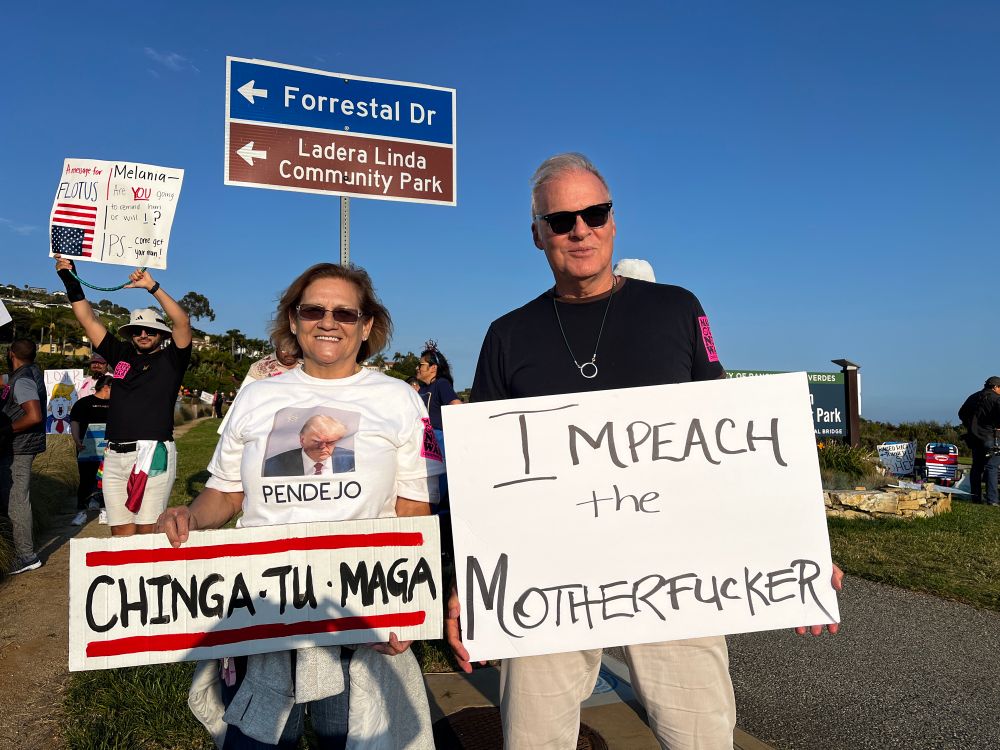 A man holding a sign that says impeach the motherfucker and a woman holding a sign that’s says Chinga tu Maga
