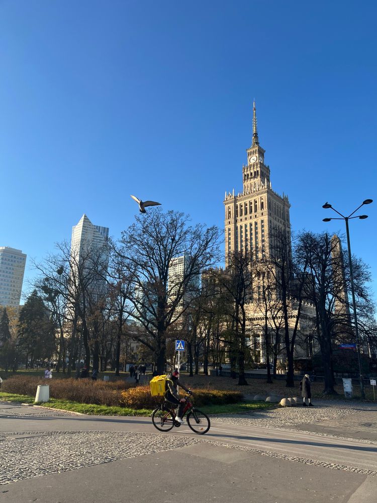 Bild des Kulturpalasts in Warschau bei Sonnenschein und mit Radfahrer.