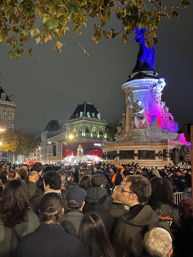 Bild von den vielen Menschen auf der Place de la République. Recurs die Marianne in Blau-Weiß-Rot und im Hintergrund eine große Leinwand.