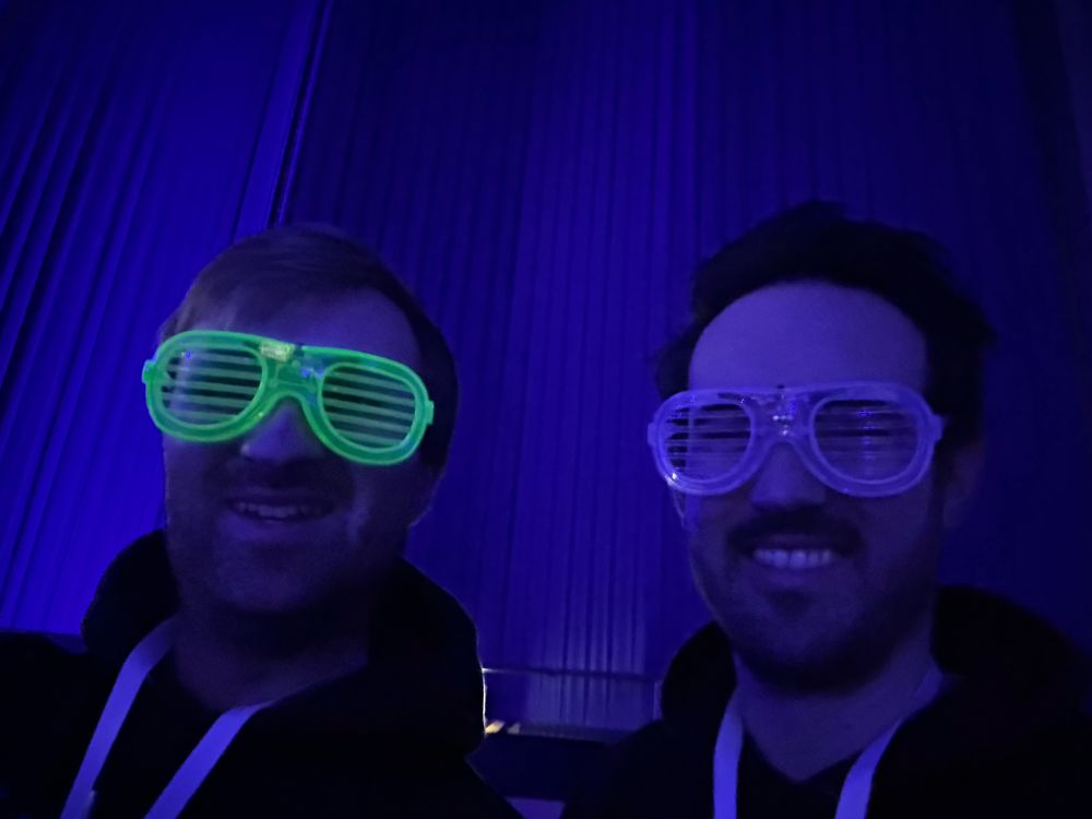 Two guys wearing luminous glasses that are glowing in the neon light