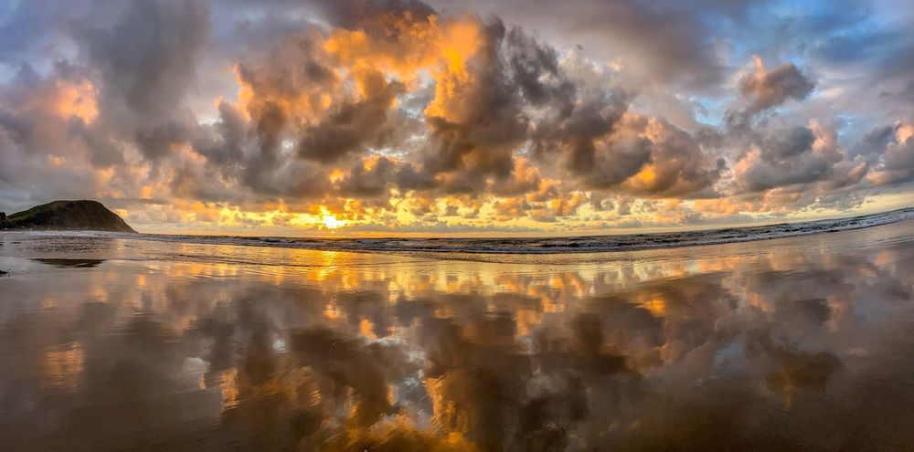 Wide angle sunrise with orange colored clouds reflected on a glassy beach. 