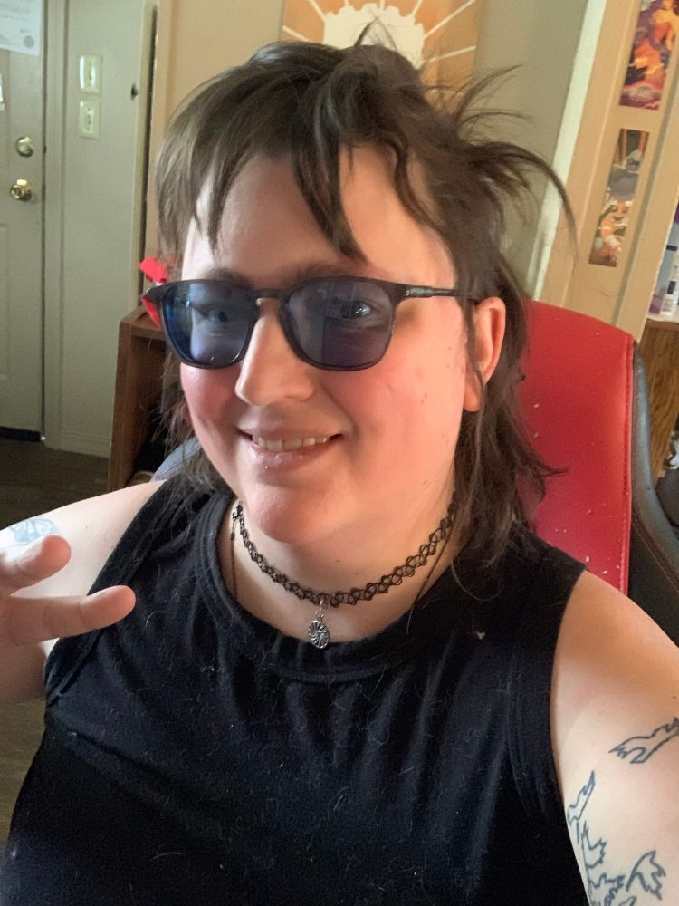 Woman smiling, making peace sign, with dark messy hat and dark glasses