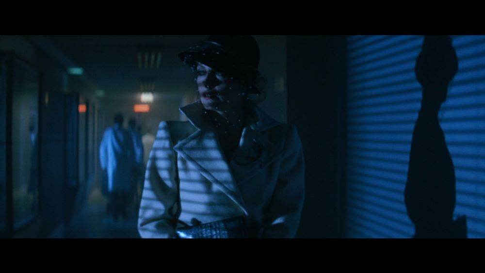 Catherine Deneuve walking down a hallway wearing a stylish white coat