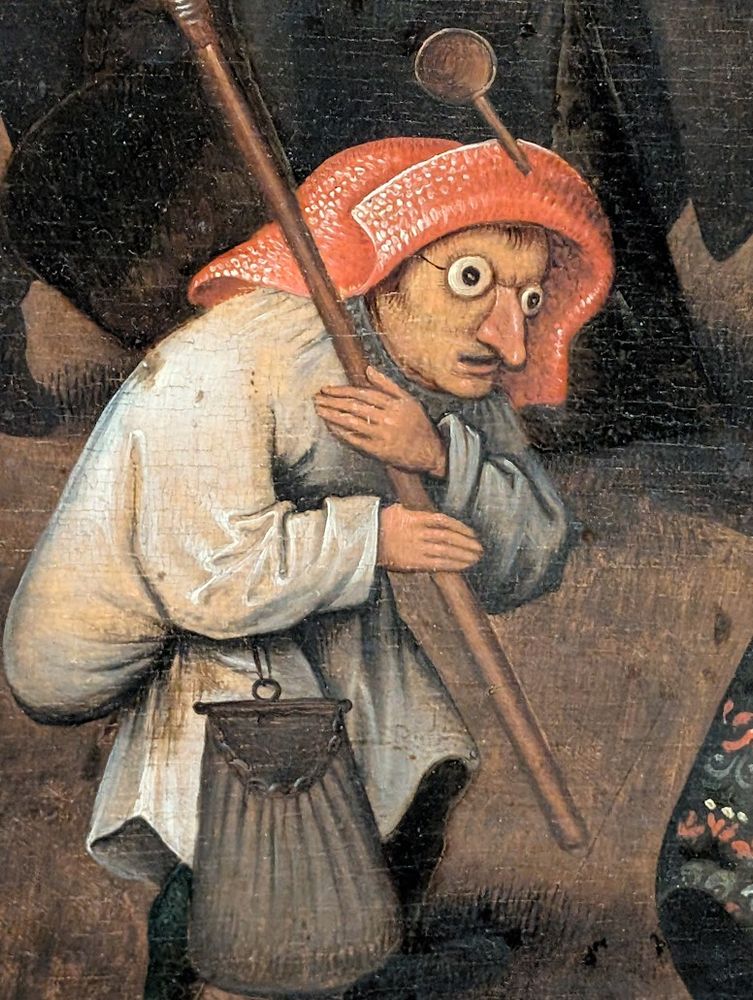 Cette image montre un autre détail du tableau "Le Combat entre Carnaval et Carême" de Pieter Bruegel l'Ancien (1559). On y voit un personnage appartenant au camp du Carnaval, facilement reconnaissable à son déguisement comique.
Le personnage porte un bonnet rouge-orange et des vêtements simples en tons beiges et gris. Ce qui frappe immédiatement, ce sont les faux yeux exorbités et le faux nez qu'il arbore, accessoires typiques des mascarades carnavalesques de l'époque. Ces éléments de déguisement lui donnent une expression grotesque et théâtrale caractéristique des festivités de Carnaval.
Ce personnage masqué illustre parfaitement l'esprit de transformation et de mascarade propre au Carnaval, où les apparences sont inversées et où le grotesque côtoie le comique. Il s'inscrit dans la tradition des déguisements et des parodies qui caractérisent cette période de liberté et d'excès précédant le Carême dans l'allégorie de Bruegel.