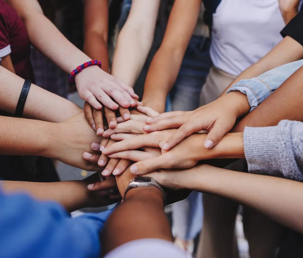 Bild mehrere Kinder verschiedeńer Hautfarbe die die Hände aufeinanderlegen.