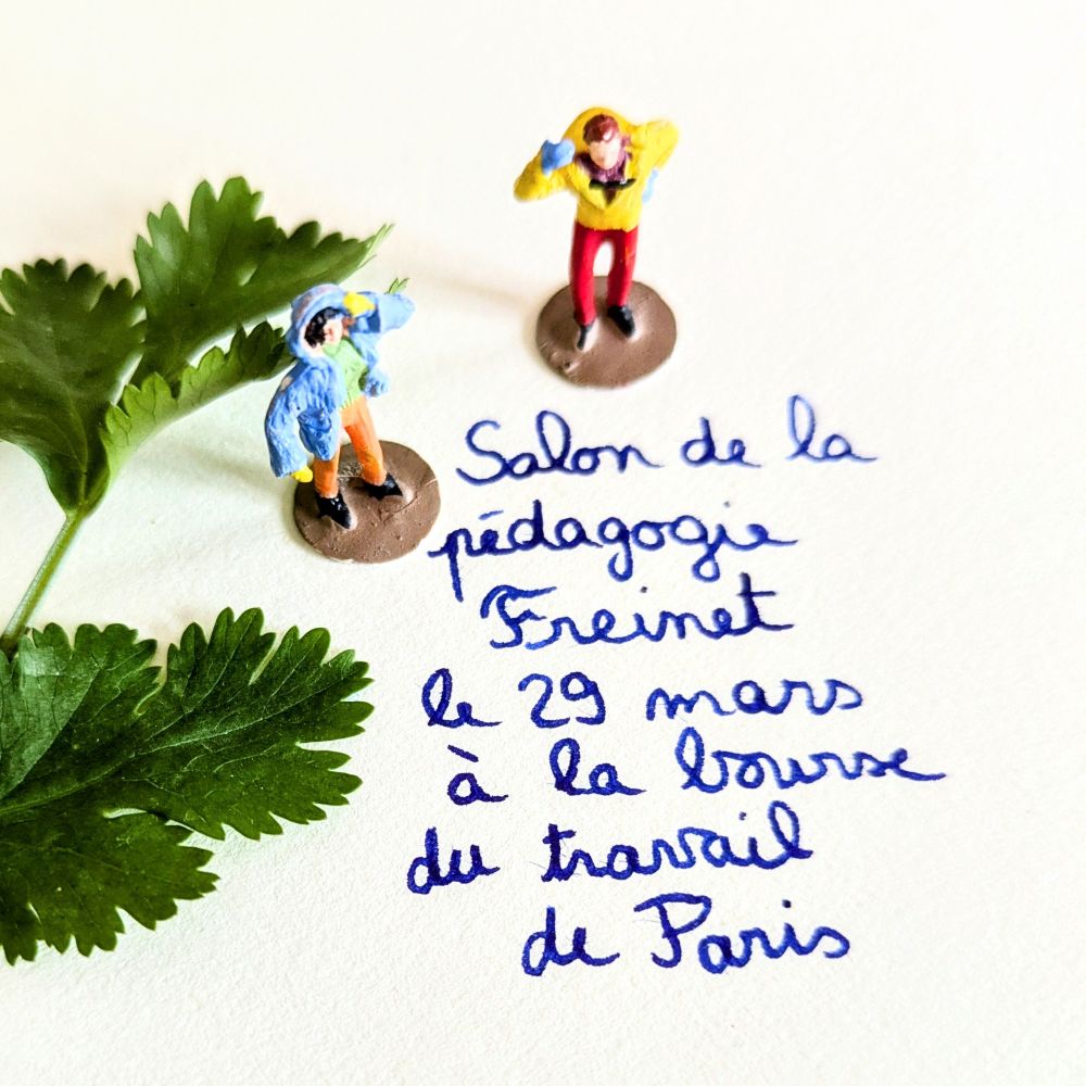 Écriture cursive bleue "salon de la pédagogie Freinet" avec deux figurines de bonhomme et une feuille de coriandre.