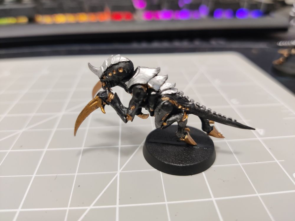 Close up picture of a Hormagaunt from Warhammer 40K, its body painted black, its carapace painted silver, and its exposed cartilage and bone painted gold