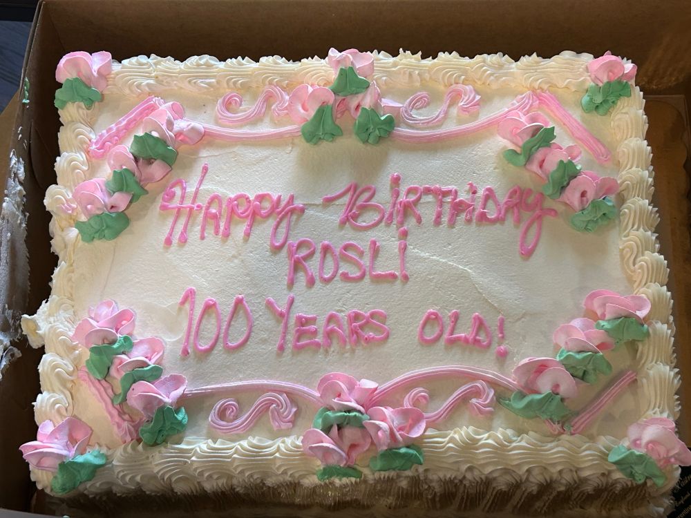 A red velvet, double layer white frosted caked with pink rose icing, reading “Happy Birthday Rosli, 100 Years Old!”
