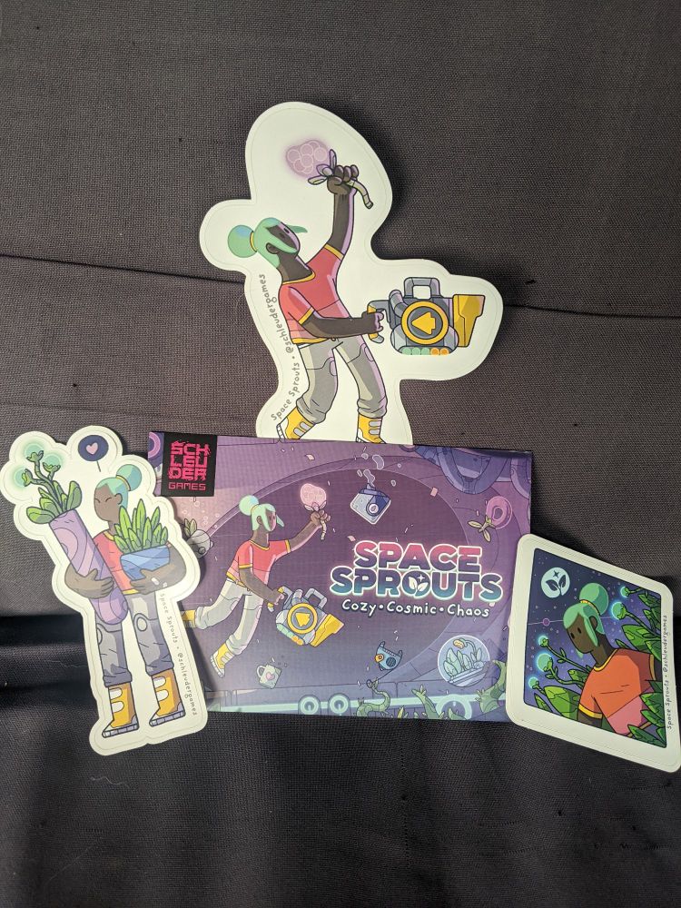 Picture of a postcard sized key art from Space Sprouts surrounded by three stickers featuring the main character, Oda, doing various activities. For one she is holding two plants with a heart over her head. For another she is floating while holding a vacuum and a plant. The third is diamond shaped and features Oda sitting in a field of plants with blue puffs at the top. The moon has a little sprout on its face. 