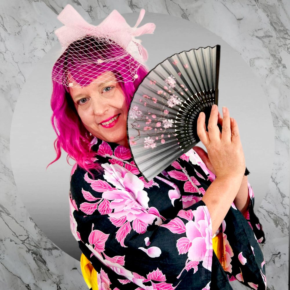 Pink haired model in kimono holding a black to grey ombre hand fan with pink Sakura flowers