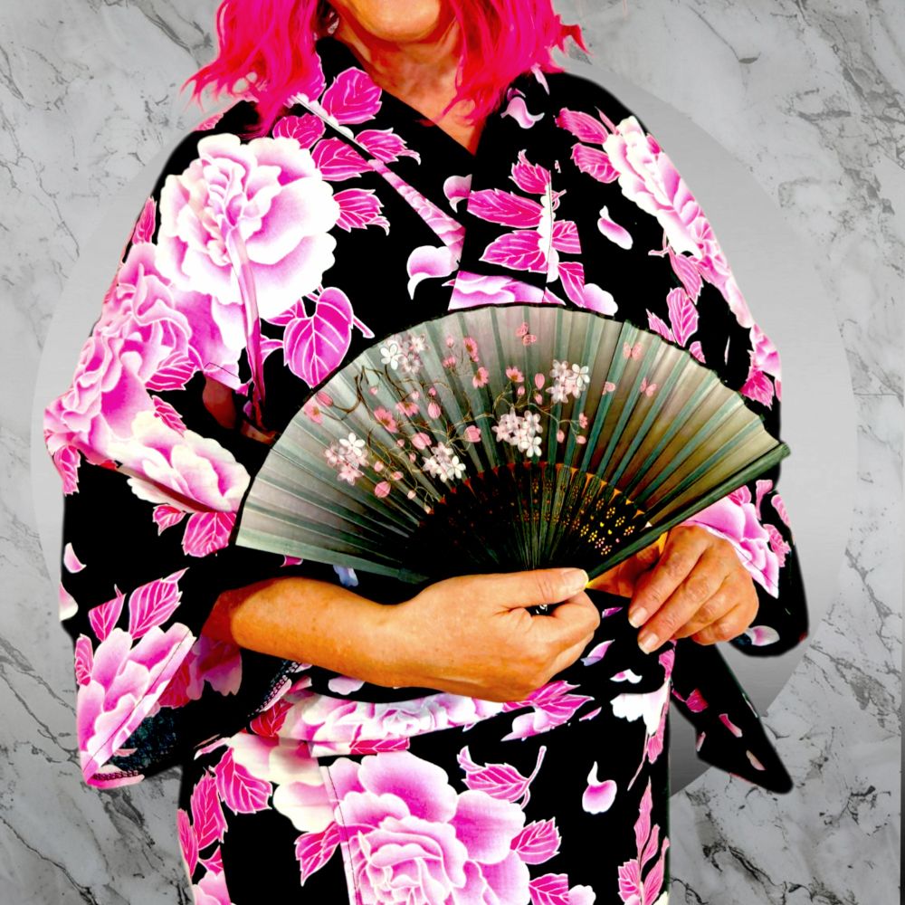 Pink haired model in kimono holding a black to grey ombre hand fan with pink Sakura flowers
