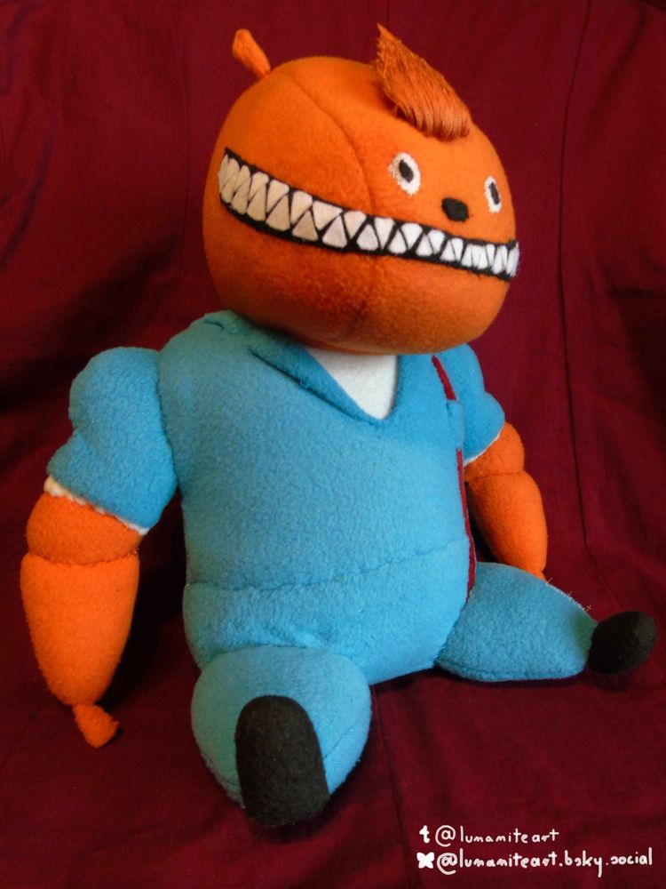 A plush doll of the bright orange monster Glottis (from the game Grim Fandango). He is grinning broadly and his bright blue jumpsuit looks impeccably clean. By lumamiteart!