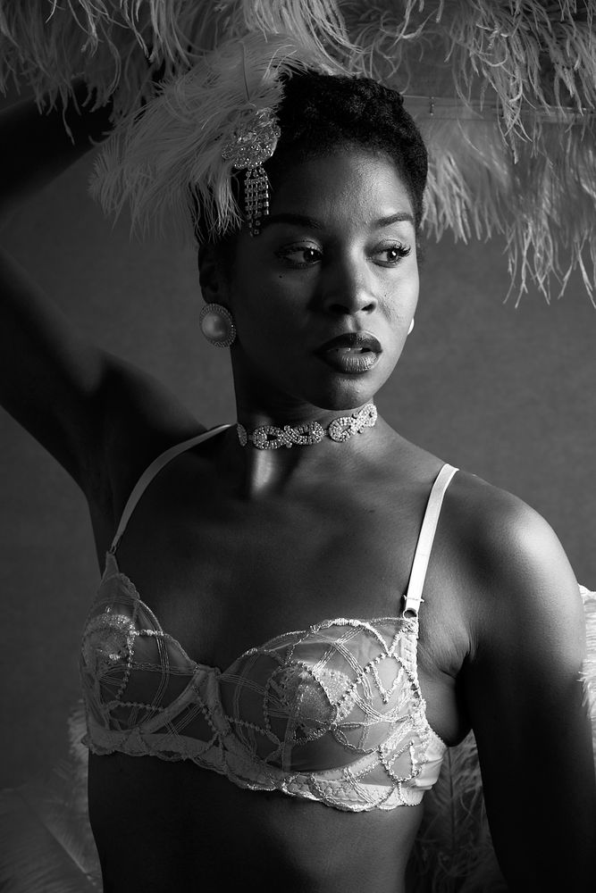 Monochrome photo of North Carolina based burlesque performer Miss Candice. It is a tightly framed portrait and she is holding a feathered above her head. 