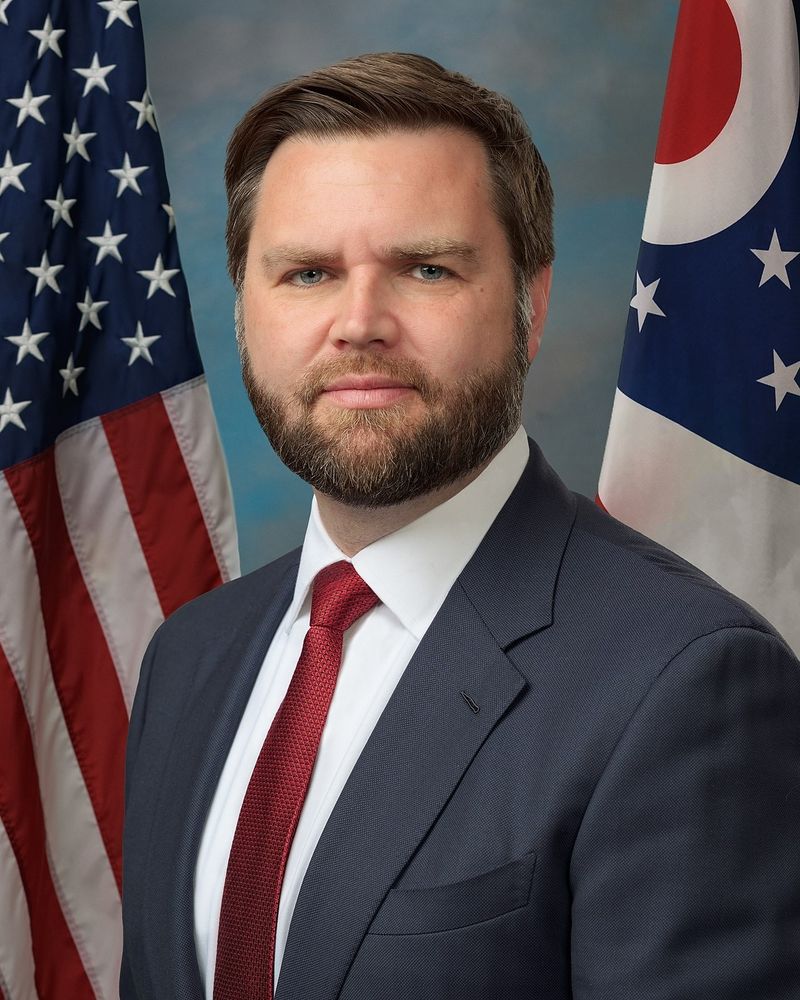 Ein Foto von JD Vance im Anzug vor zwei amerikanischen Flaggen