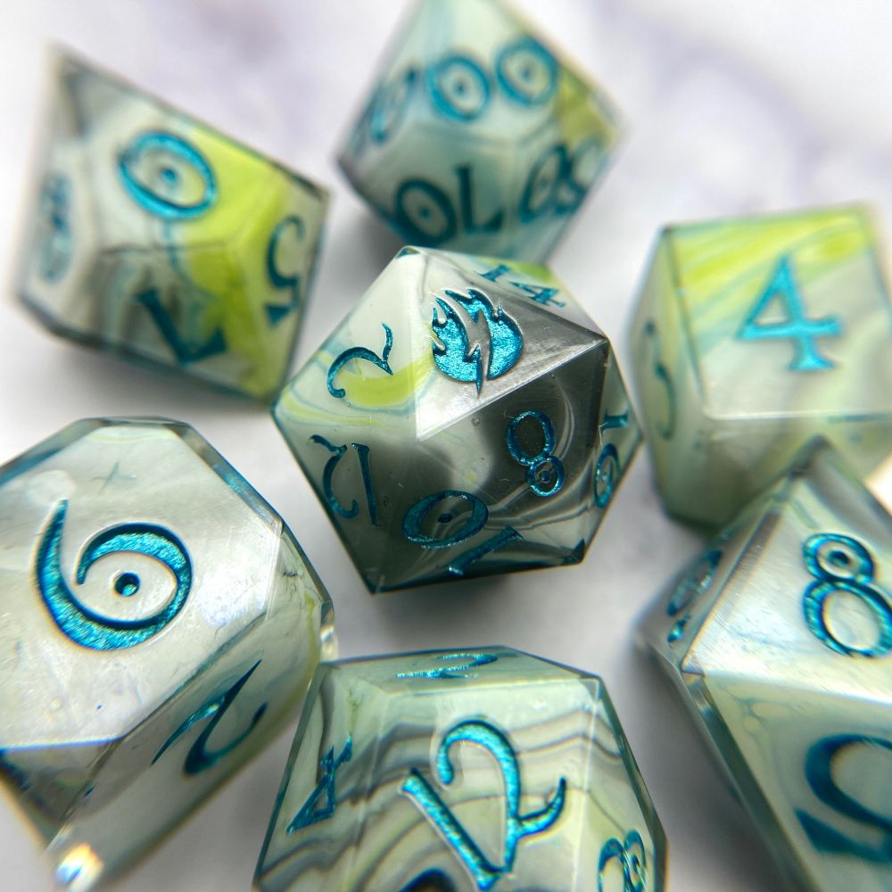 A set of dice that has a white base, with swirls of black, lime green, and teal blue, inked in a metallic teal. 