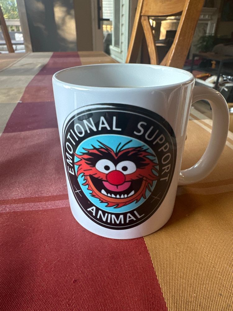A coffee mug with a picture of Animal from The Muppets and the text “Emotional support Animal.”