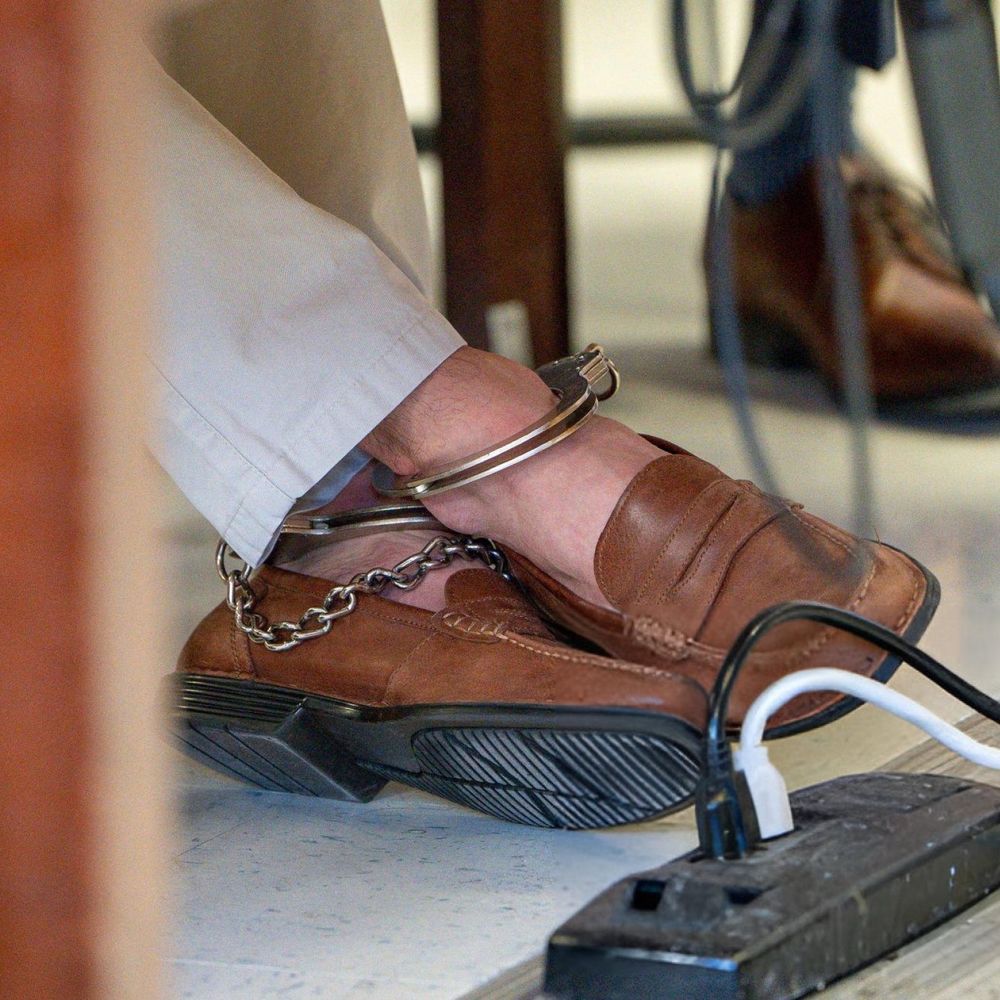 A photo of Luigi Mangione’s feet crossed in fancy-looking leather shoes with handcuffs around his crossed ankles