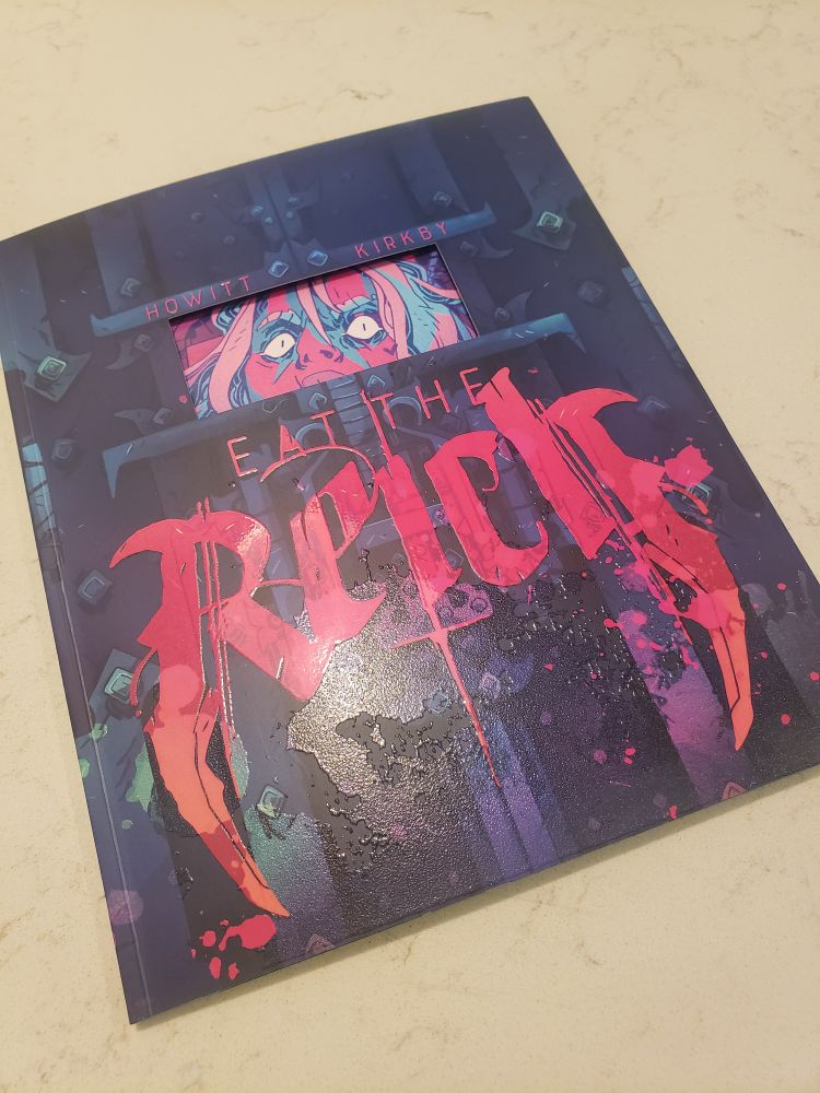 A picture of the TTRPG rulebook for "Ea Ltd the Reich," an independent TTRPG where you play a squad of vampire commandos on a mission to kill Hitler.

The cover features the title in stylish, pink font, and a cut out box to see the page beneath it, which is the image of a crazed face staring wide-eyed out of the box.