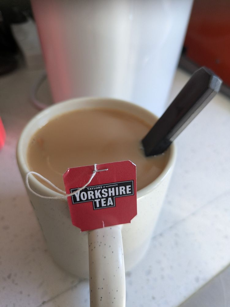 A close up of a "cuppa tea", a mug of black tea from Taylor's of Harrogate in Yorkshire as shown on the red tag of the teabag, with the milk a ruddy colour from an extended brewing time
