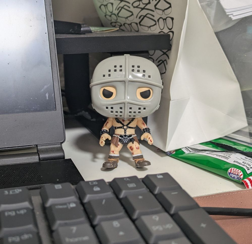 A photo of the author's writing buddy, a Funko Pop vinyl figurine of The Humungus from the movie Mad Max 2 aka The Road Warrior.

The Humungus is a bare chested man wearing bondage straps and a colander- like metal face mask, with cancerous sores on his body.

He is introduced in the movie by his herald, "Greetings from The Humungus. The Lord Humungus. The Warrior of the Wasteland. The Ayatollah of Rock'n'Rollah."