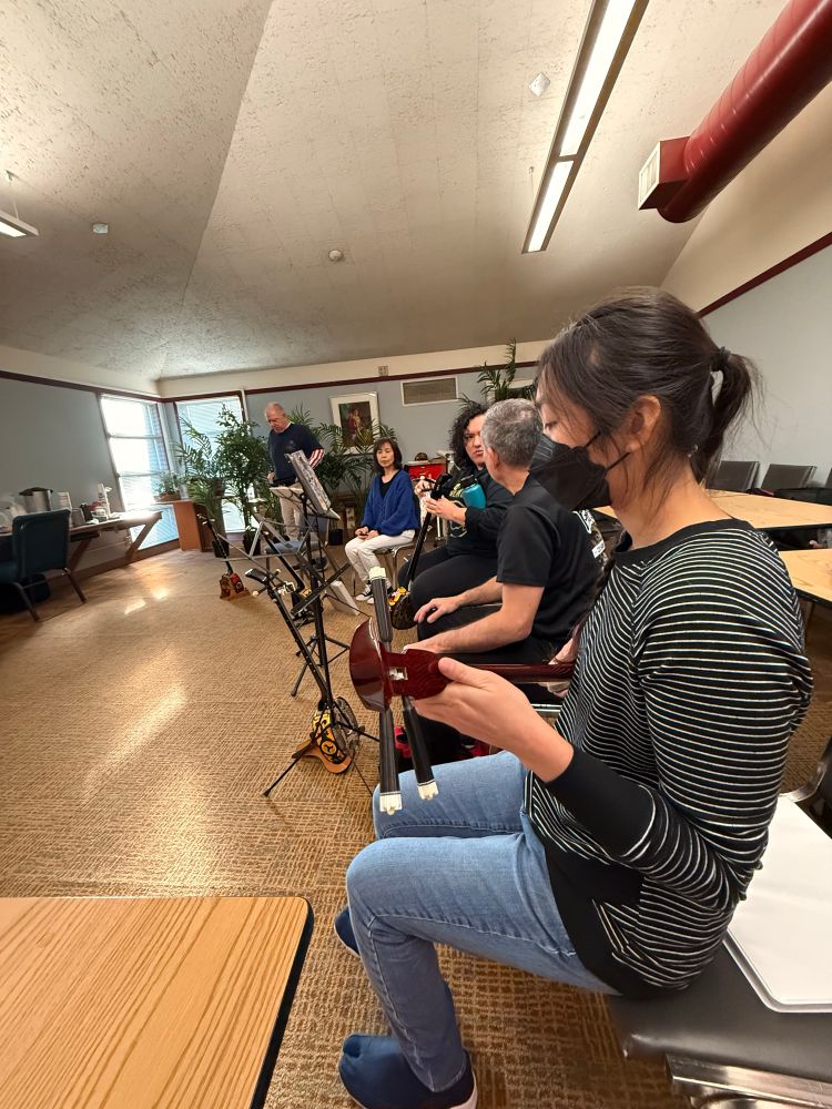 An assortment of people with Sanshins and music stands in a room