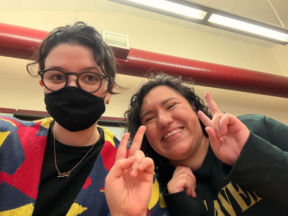 An Okinawan guy with a mask and a necklace that reads “Uema” holding a peace sign next to a smiling woman with a peace sign