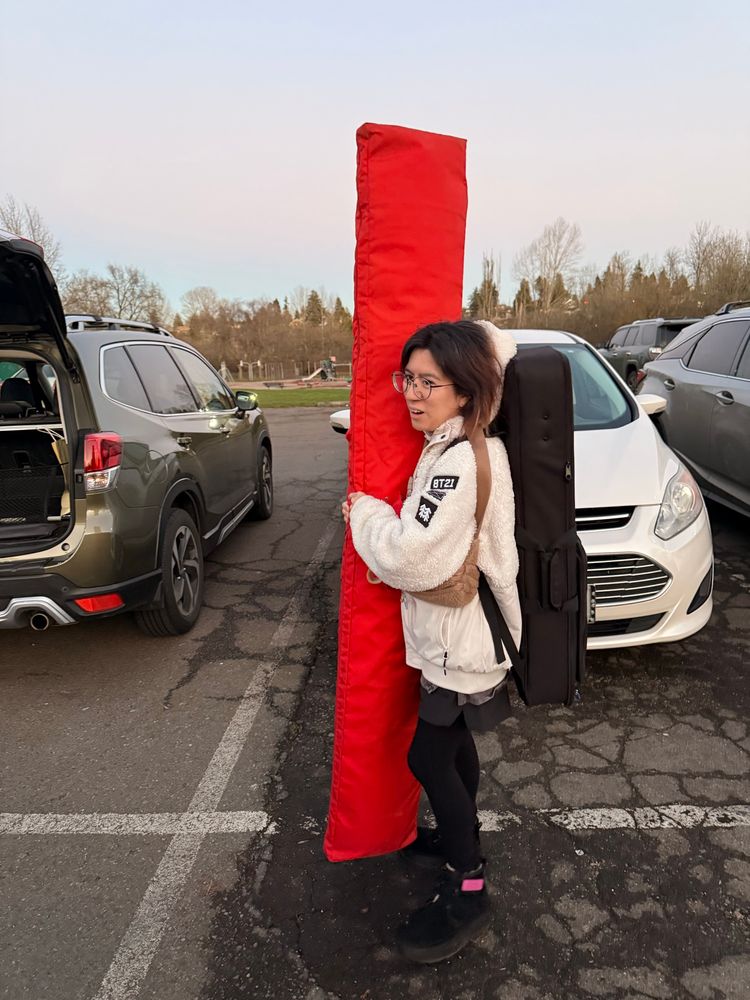 An Okinawan woman holding up an instrument case that is comically larger than her