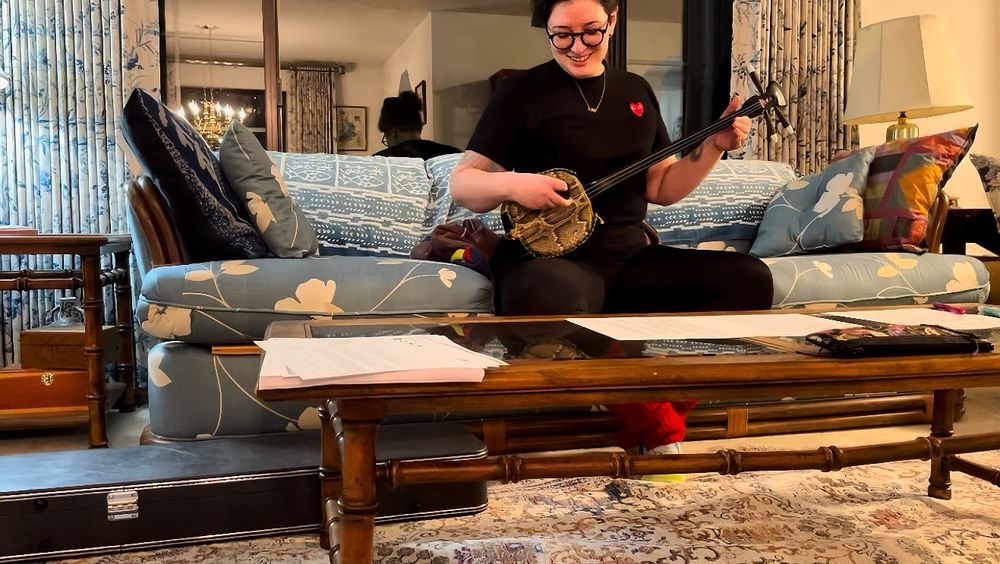 A guy looking down at a glass coffee table with a sanshin in his hands
