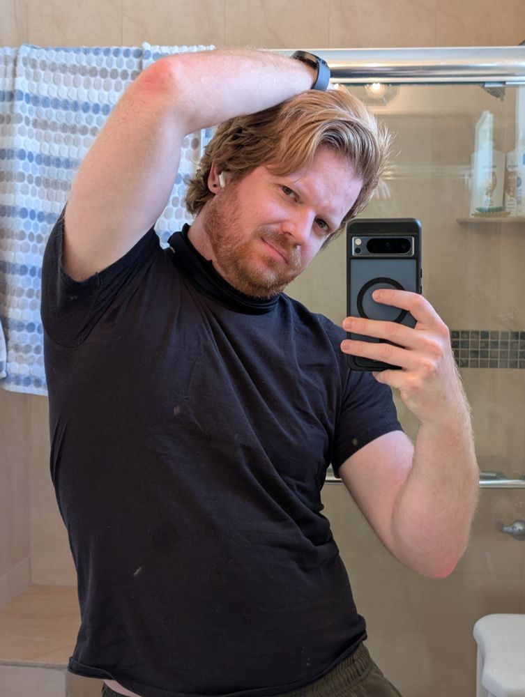 Scooter taking a mirror selfie raising his arm over his arm slightly smirking