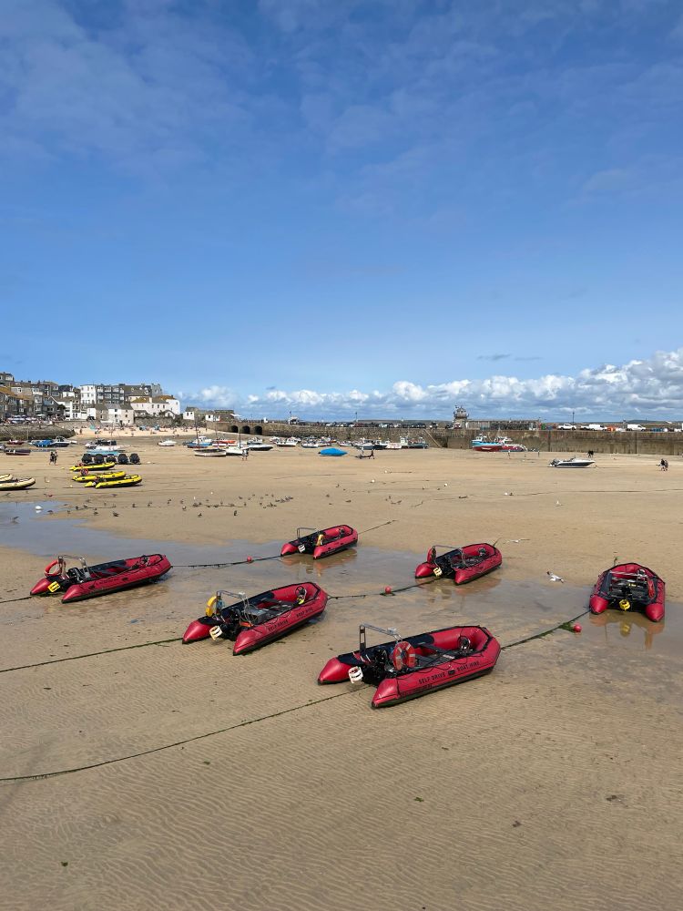Sechs rote Motorboote verbunden mit Seilen bei Ebbe auf dem Meeresgrund in St. Ives, Großbritannien. 