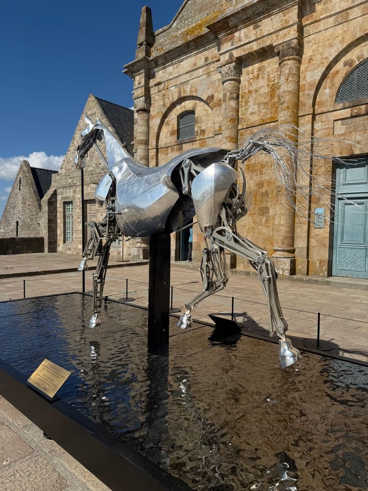 Foto von der Skulptur: Im Mont-Saint-Michel könnt ihr aktuell das berühmte mechanische Pferd bestaunen, welches bei der olympischen Eröffnungsfeier mit einer silbernen Reiterin und der olympischen Flagge auf den Schultern auf der Seine die ganze Welt in ihren Bann zog. Unter der riesigen Kapuze verbarg sich Morgane Suquart, Mitbegründerin von MMProcess, die dieses spektakuläre Schlachtross nicht nur entworfen, sondern auch geritten hat.