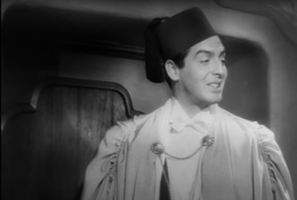 Victor Mature looking suave in a fez and some sort of fancy flowing gown over his white tie