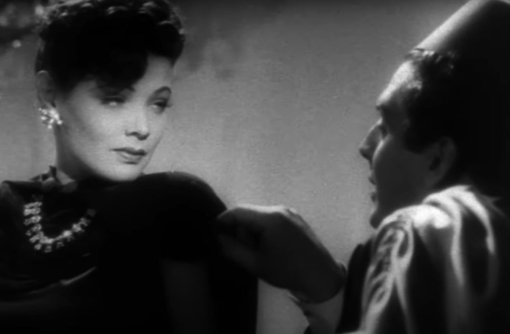 Gene Tierney, still supernaturally beautiful,  talking to Victor Mature, still in the fez and gown