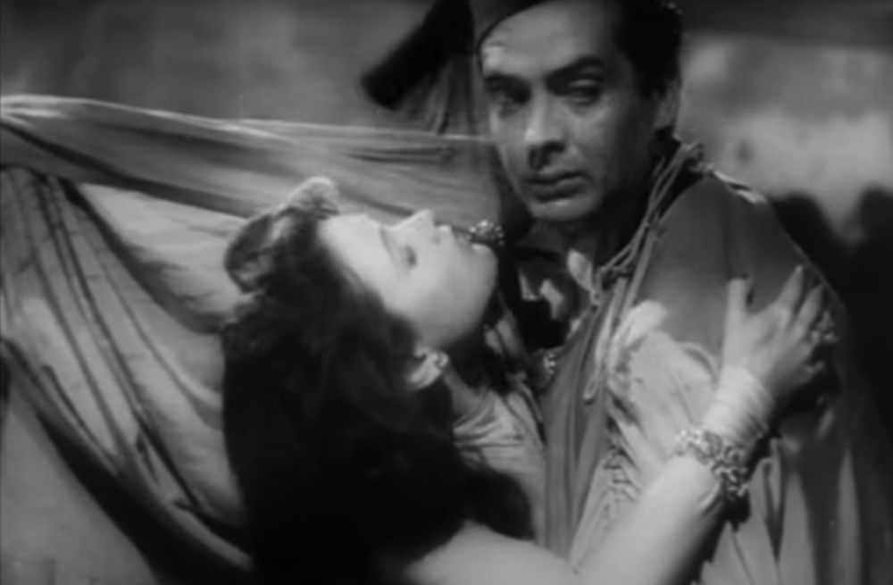 Victor and Gene in a clinch. He's raising up his gown as a screen before going in for a kiss
