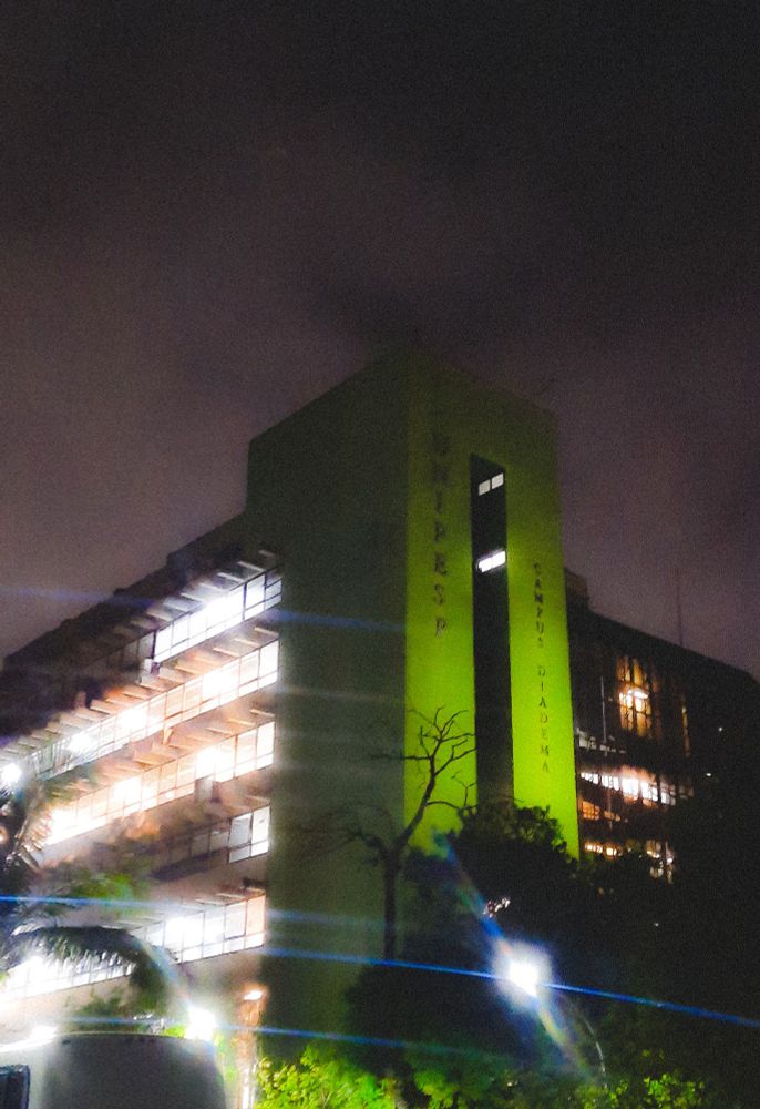 Prédio com janelas de vidro e uma coluna verde com as luzes acesas de noite