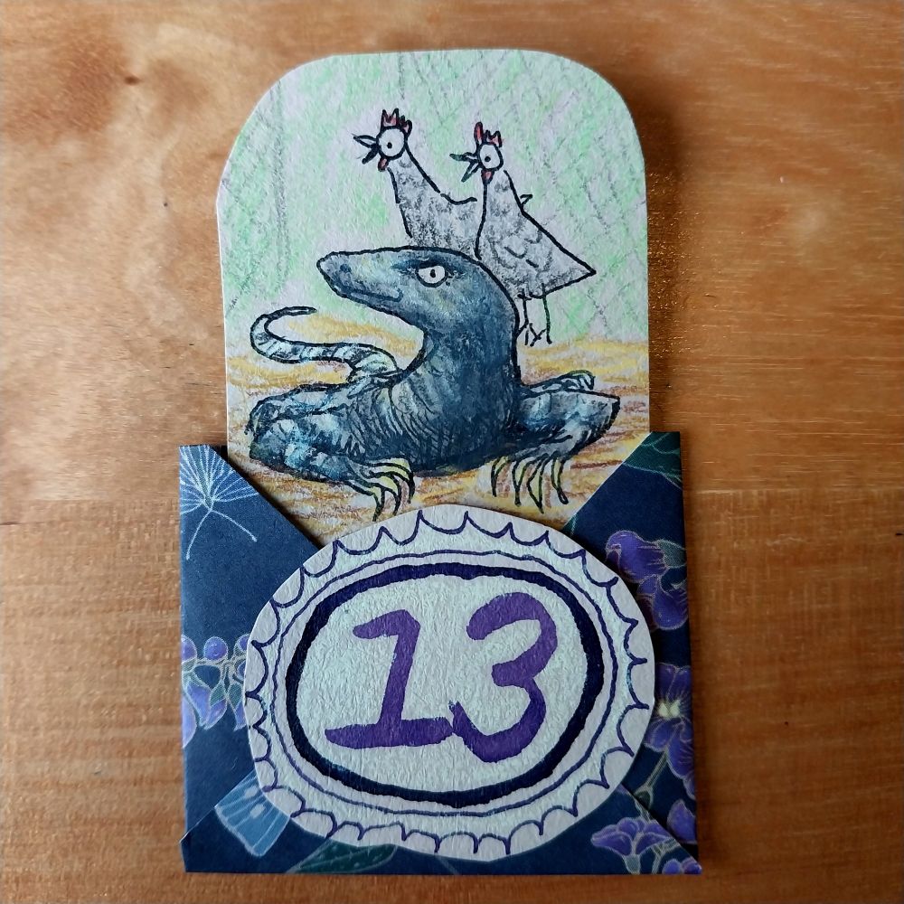 Photo of a square envelope, made with decorative purple and black paper, with a large hand-drawn number 13 on the front. It is open at the top to slot in a drawing. The drawing is of a Lace Monitor (large lizard) with two hens in tha background looking alarmed.