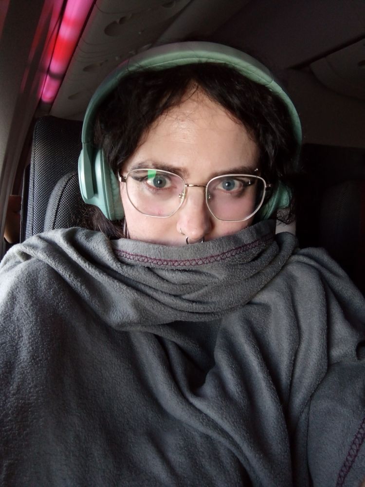 Selfie en el avión con cascos azules de música y tapada con una manta gris