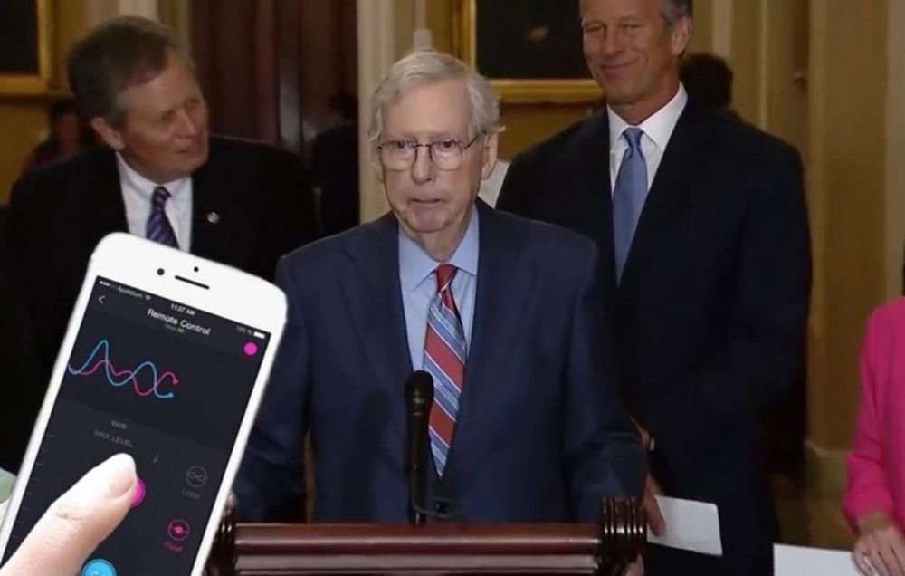 Mitch McConnell frozen, unable to speak and eyes glazed over while a photoshopped cutout of a finger and a phone. On the phone screen appears to be an app designed for Bluetooth controlled sex toys being interacted with said finger. 