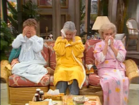 Blanche cover her eyes in her night dress, Dorothy covering her ears in her robe with a Kleenex and Rose blowing her nose in her robe while they are all sick on the couch