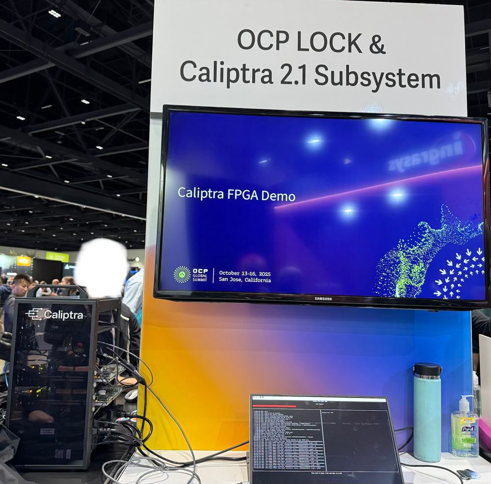 Mini rack with FPGA boards and blinking lights that says “Caliptra” on the side. A TV with a slideshow that says “Caliptra FPGA Demo”. A monitor that has a terminal scrolling a bunch of text that is hard to read but looks technical.