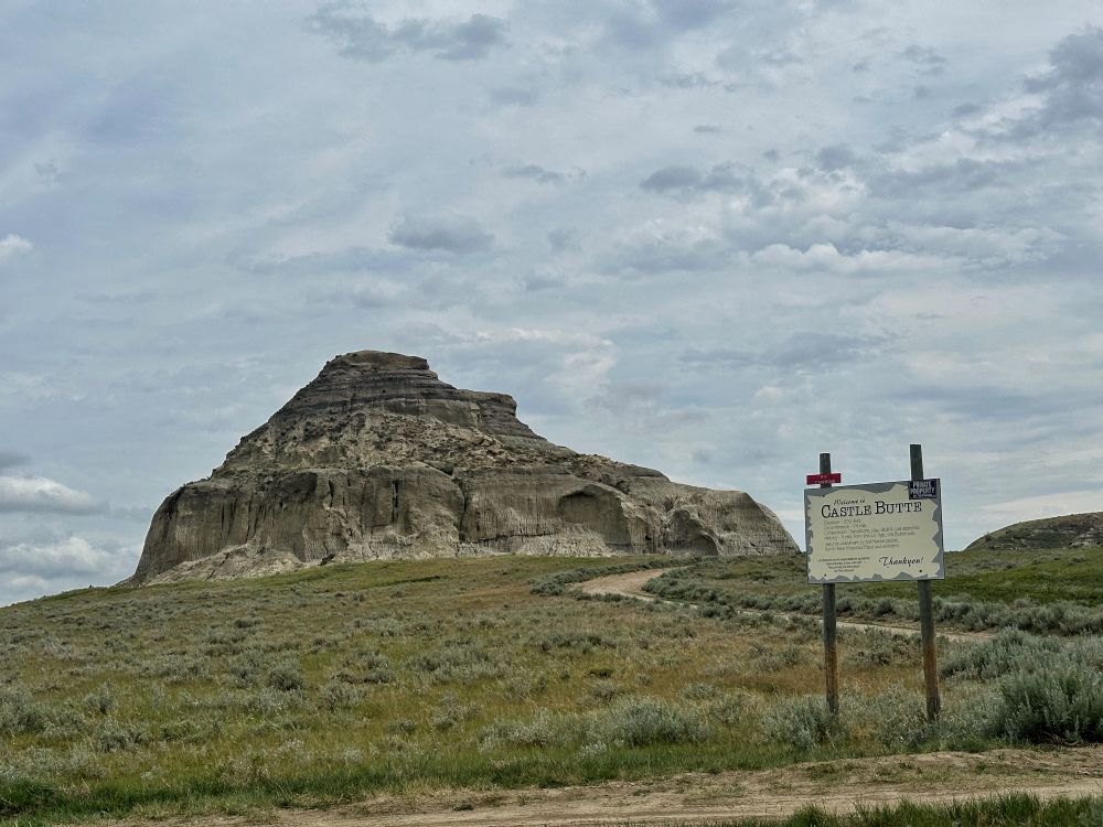 A view of castle butte showing its steep walls along the base as it stands sentinel over the sagebrush. A sign shares its vital statistics - 60 metres tall, half a kilometre around. 