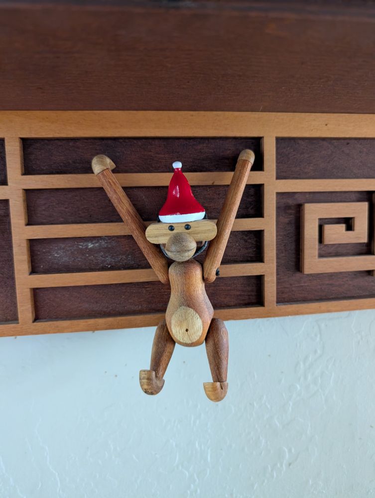 A tiny wooden monkey wearing a Santa hat