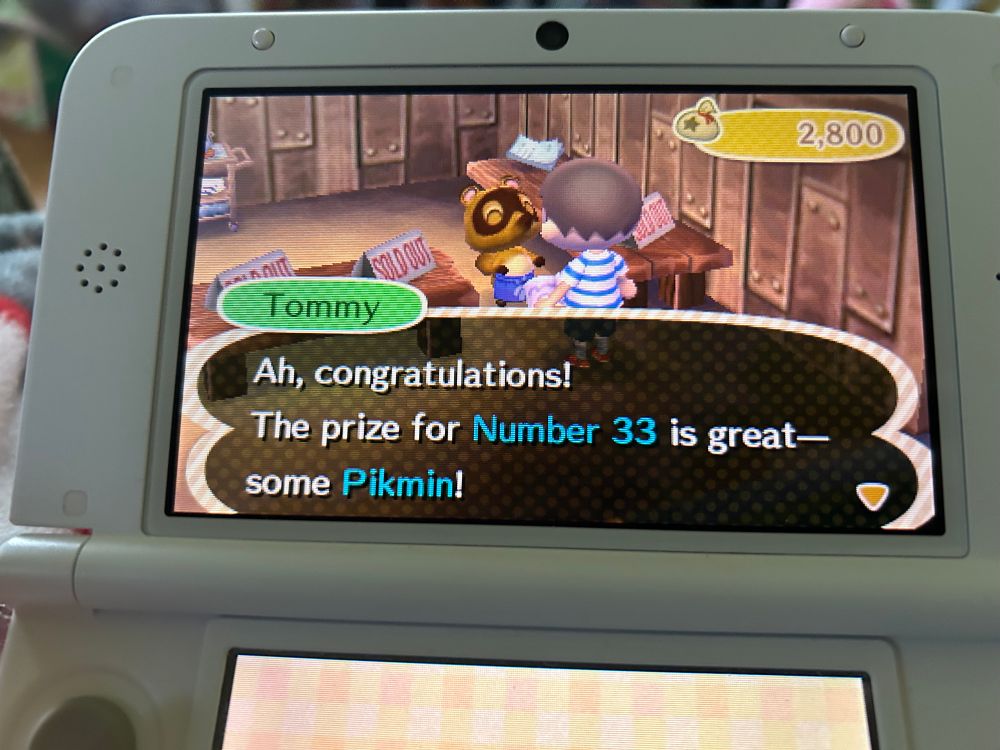A picture of my White 3DS XL displaying Animal Crossing New Leaf. I am inside Nookling Junction talking to Tommy, who says “Ah, congratulations! The prize for Number 33 is a great- some Pikmin!”