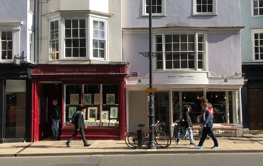 A street scene in Oxford, with pedestrians and shops, with late afternoon sunlight. 