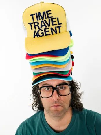 Judah Friedlander wears a stack of hats on his head. The top one says TIME TRAVEL AGENT